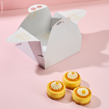 Scatola porta torte bianca aperta e 3 pasticcini di fronte